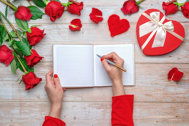 Mani femminili in maniche rosse pronte a scrivere in un quaderno a quadri con copertina rigida