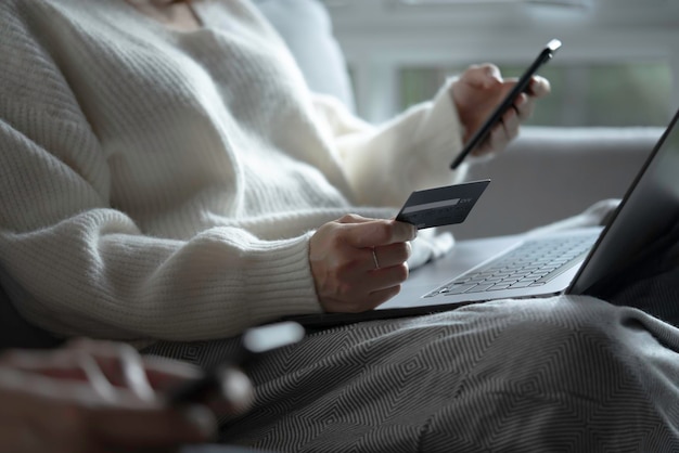 Mani femminili in possesso di carta di credito utilizzando smartphone e laptop Acquisti online