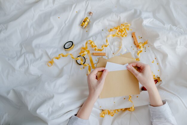 Mani femminili in possesso di carta regalo, busta e confezione regalo sopra la coperta del letto. Concetto di Natale e Capodanno. Vista orizzontale superiore