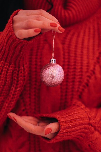 Mani femminili in un maglione invernale lavorato a maglia che tiene una palla di Natale scintillante rosa Dettagli di Capodanno