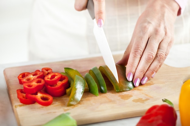 Mani femminili senior Taglio dei peperoni verdi sul bordo della cucina.