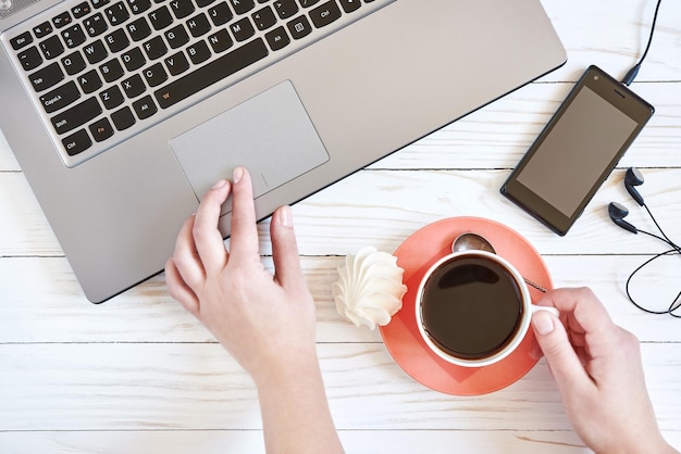 Mani femminili sulla tastiera del computer portatile e sul primo piano della tazza di caffè