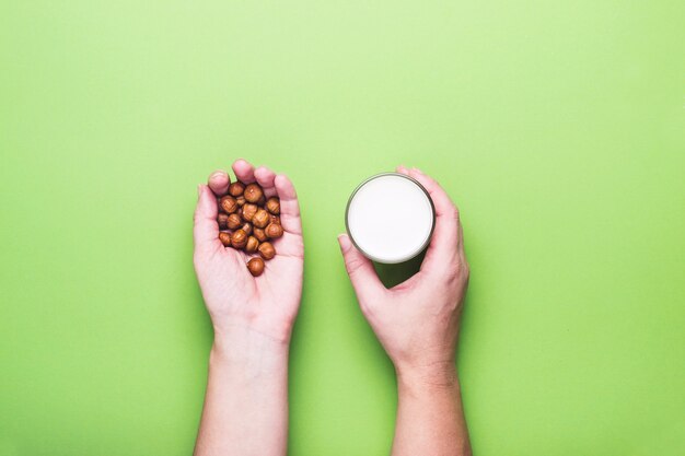 Mani femminili Tiene nocciole e un bicchiere di latte senza latticini.