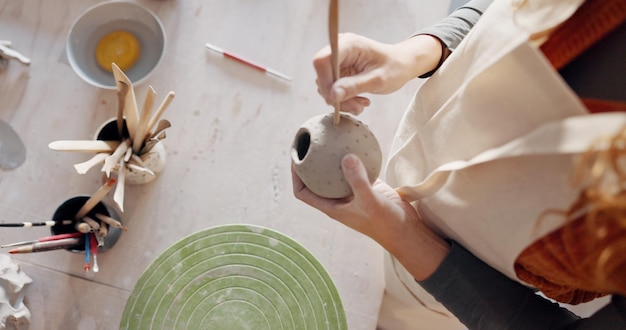 Mani in ceramica fango o scultore artista con tazza di argilla tazza o vaso in laboratorio di produzione di prodotti in studio d'arte o piccola impresa Vista dall'alto donna e strumento di scultura in negozio creativo o classe di ceramica