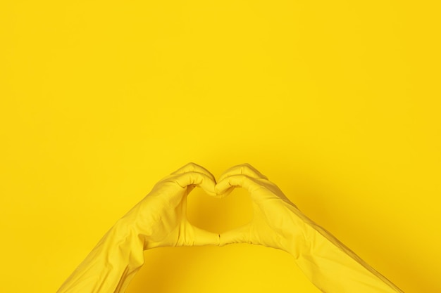 Mani in guanti che fanno a forma di cuore su sfondo giallo, concetto di pulizia dell'amore