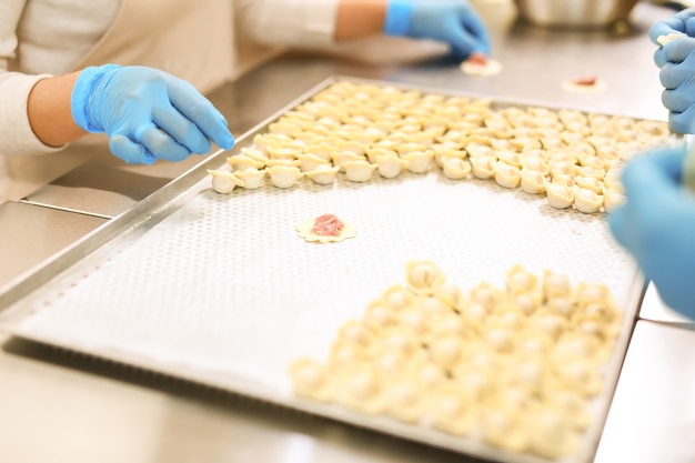 Mani in guanti di gomma blu e gnocchi su vassoio ricoperto di carta oleata Industria alimentare