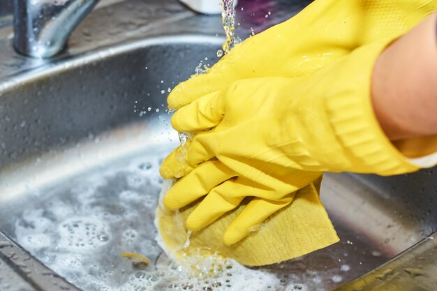 Mani in guanti gialli che puliscono lavandino nella cucina