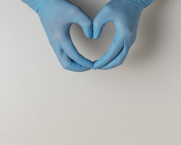 Mani in guanti medicali a forma di cuore su bianco con copia spazio.