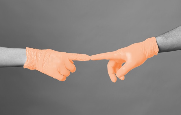 Mani in guanti medici allungate l'una all'altra contro uno sfondo grigio