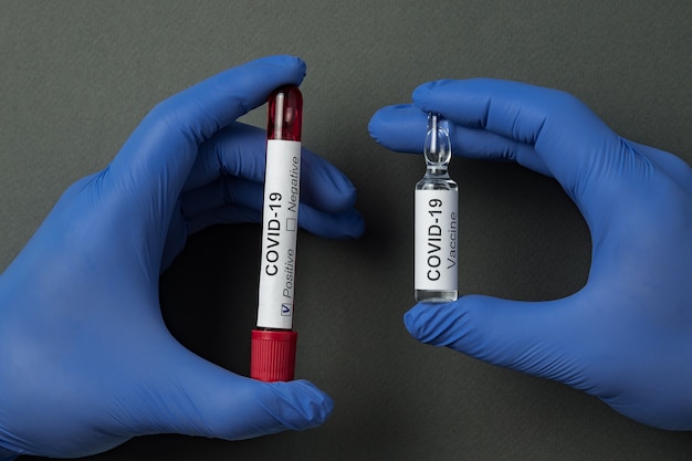 Mani in guanti medici che contengono campione di sangue e fiala di vaccino di Covid-19. Trattamento da virus corona