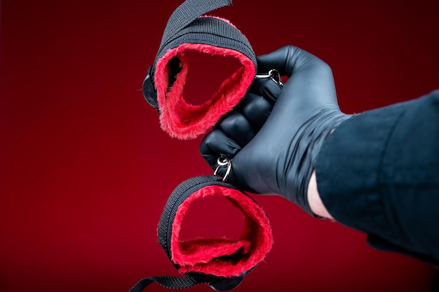 Mani in guanti neri che tengono le manette con cinture rosse per giochi sessuali bdsm