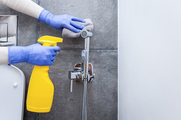 Mani in guanti protettivi che puliscono la doccia igienica nella stanza sanitaria