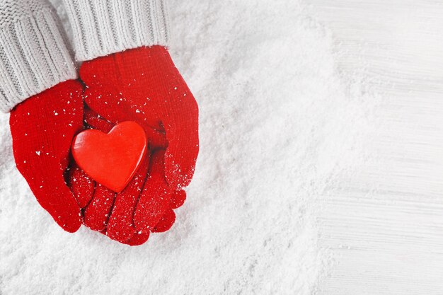 Mani in guanti rossi caldi che tengono il cuore su sfondo innevato