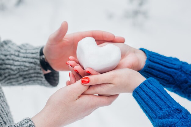 Mani in guanti tricottati con cuore di neve nel giorno di inverno. Concetto di amore. Giorno di San Valentino.