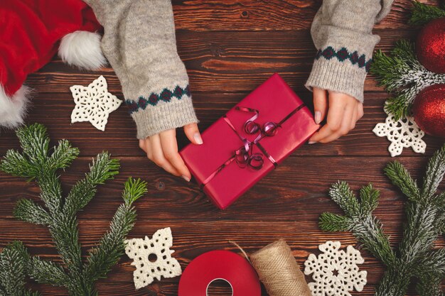 Mani in maglione che tiene un regalo sulla tavola di legno con le decorazioni di Natale