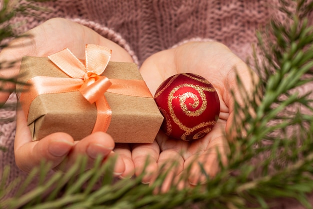 Mani in un maglione lavorato a maglia che tiene la confezione regalo. Concetto di preparazione vacanze di Natale.