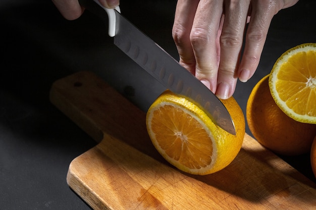 Mani irriconoscibili della donna che tagliano fette di arancia fresche e sane sul bordo di legno