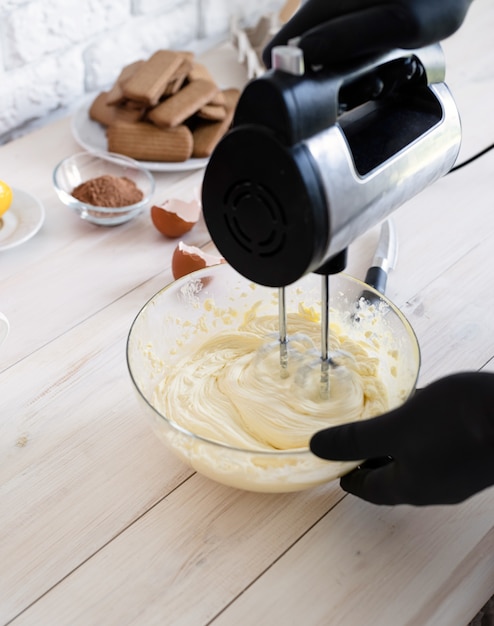 Mani maschii che mescolano la pasta con il miscelatore elettrico in un primo piano della cucina