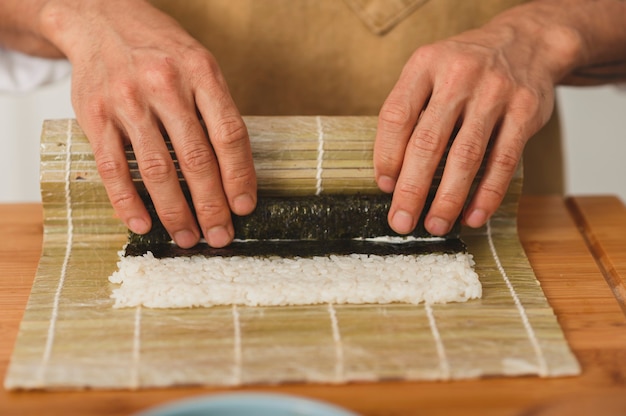 Mani maschii chef chiudono il processo di rotolamento sushi nori e riso bianco