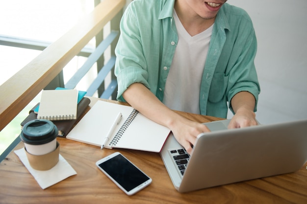 Mani maschii di affari che scrivono su una tastiera del computer portatile sullo scrittorio con una tazza di caffè in Li di sera