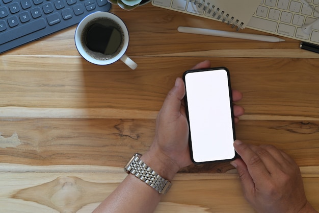 Mani maschii facendo uso del modello dello schermo in bianco dello smartphone alla scrivania