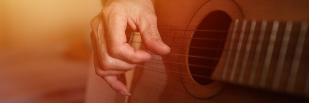 Mani maschili anziano uomo caucasico anziano che tiene e suona la chitarra classica da vicino a casa chitarristi senza volto non professionali le persone suonano musica amatoriale hobby domestici e bagliori di striscioni per il tempo libero