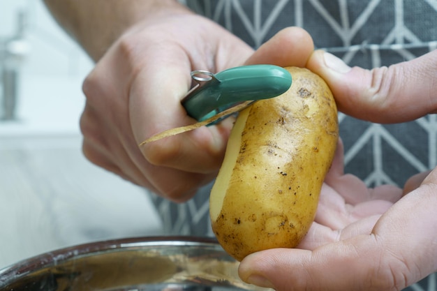 Mani maschili che sbucciano patate fresche con pelapatate sopra la ciotola primo piano Rottami alimentari raccolta differenziata rifiuti zero