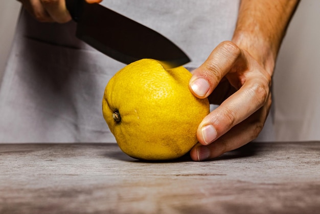 Mani maschili che tagliano un limone giallo maturo con un coltello su un tavolo di ardesia. Vista frontale.
