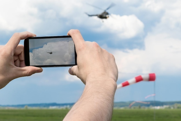 Mani maschili che tengono smartphone e fotografano l'elicottero nel cielo blu