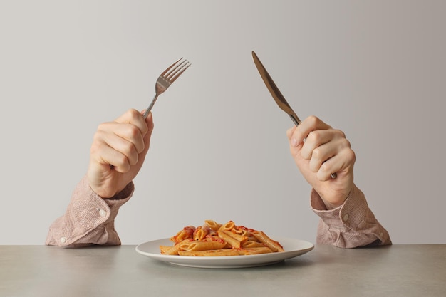 Mani maschili con coltello e forchetta accanto a un piatto di pasta con pomodori e formaggio