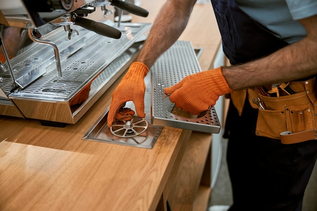 Mani maschili in guanti da lavoro che riparano la macchina da caffè