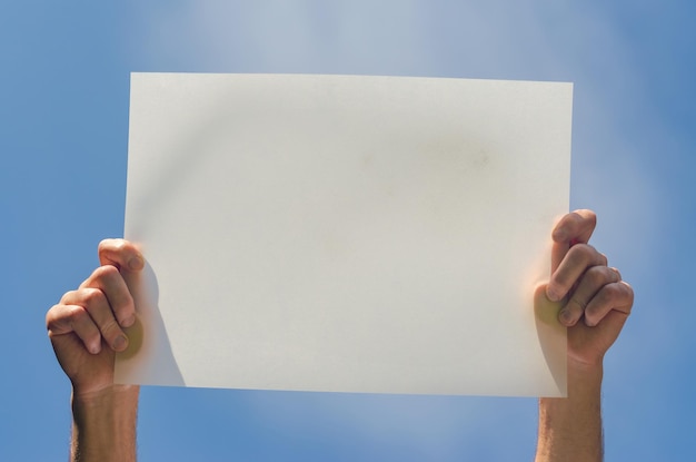 Mani maschili tengono un poster bianco vuoto sullo sfondo blu del cielo foto di alta qualità