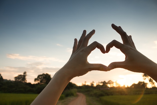 Mani nell&#39;amore di forma cuore, mano della siluetta fanno la forma del cuore con il sole