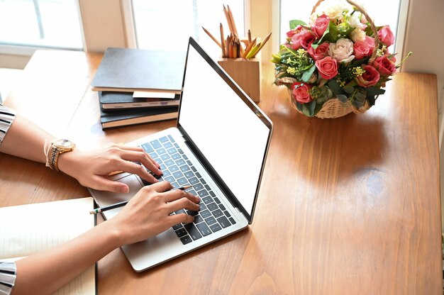 Mani potate delle donne del colpo facendo uso del computer portatile del modello sul tavolo di lavoro.