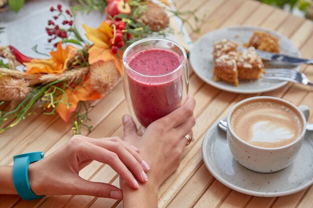 Mani sane della donna all'ora di pranzo autunnale con una tazza di caffè e un dessert di frullato alla fragola rosa tra le decorazioni autunnali