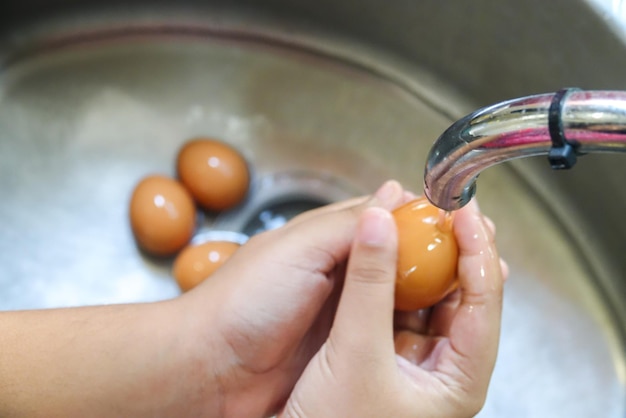 Mani tagliate che lavano le uova nel lavandino.