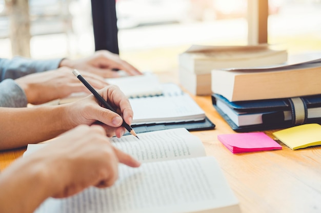 Mani tagliate di amici con libri che studiano sulla scrivania in classe