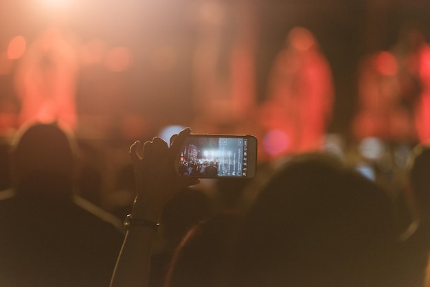 Mani tagliate di una donna che fotografa con uno smartphone a un concerto musicale