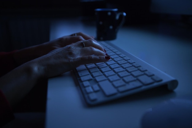 Mani tagliate di una donna che usa la tastiera di un computer sul tavolo nella camera oscura a casa