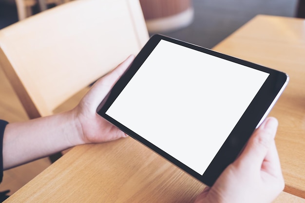 Mani tagliate di una persona che tiene un tablet digitale vuoto sul tavolo