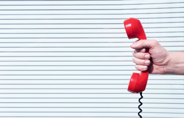 Mani tagliate di una persona che tiene un telefono rosso contro la parete