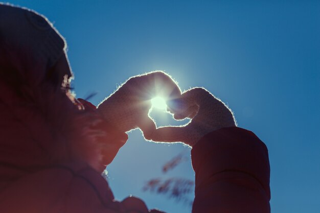 Mani umane che gesticolano un segno d'amore su uno sfondo di sole