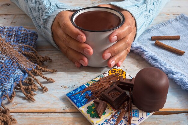 mani umane femminili che tengono una tazza di cioccolato cremosa e spessa tavolo in legno come sfondo con pezzi