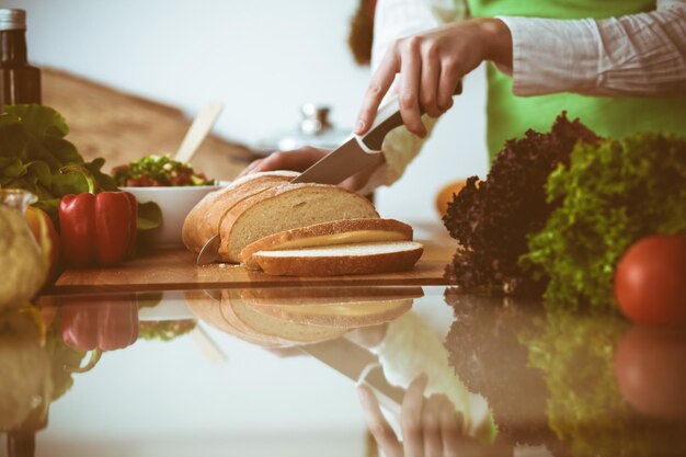 Mani umane sconosciute che cucinano in cucina. Donna che affetta il pane. Pasto sano e concetto di cibo vegetariano