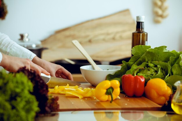 Mani umane sconosciute che cucinano in cucina. Donna che affetta il peperone dolce giallo Pasto sano e concetto di cibo vegetariano.