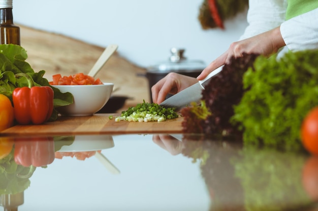 Mani umane sconosciute che cucinano in cucina. Donna che affetta la cipolla verde Pasto sano e concetto di cibo vegetariano.