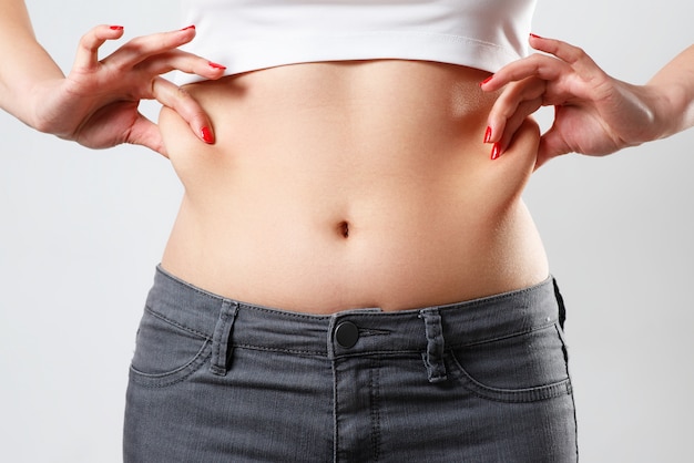 Mani una donna tiene una piega di grasso in eccesso sullo stomaco. su bianco