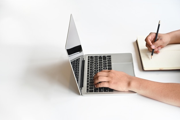 Mani usando il computer portatile e scrivendo la carta del taccuino con la tabella dello spazio della copia.