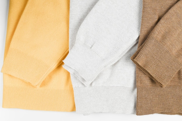 Maniche di tre di caldi diversi pullover di lana lavorati a maglia beige marrone giallo colori isolati su bianco Panno caldo in colori pastello per un look primaverile elegante Foto di alta qualità