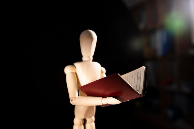Manichino in legno su sfondo nero con libro